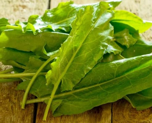 A pile of green leafy vegetables on top of a wooden table.