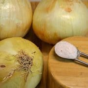Onions are sitting on a wooden board next to a spoon.