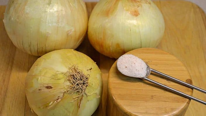 Six Hour Onion Ingredients Onions are sitting on a wooden board next to a spoon.