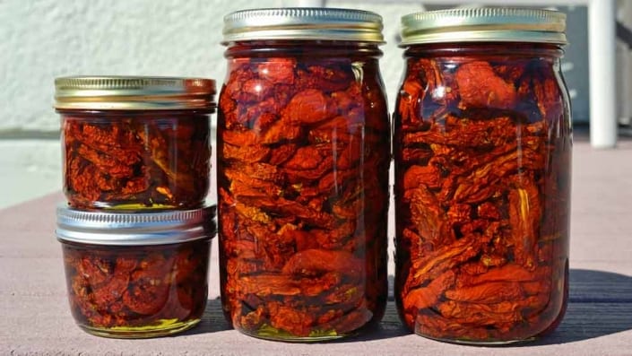 Sun Dried Tomatoes A group of jars filled with food on top of a table.