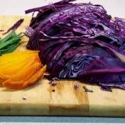 A cutting board with some purple cabbage and an orange.