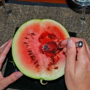 A person cutting into a watermelon with scissors.