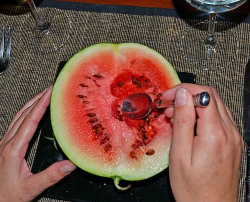 A person cutting into a watermelon with scissors.