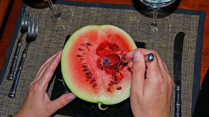 Watermelon-Dessert A person cutting into a watermelon with scissors.
