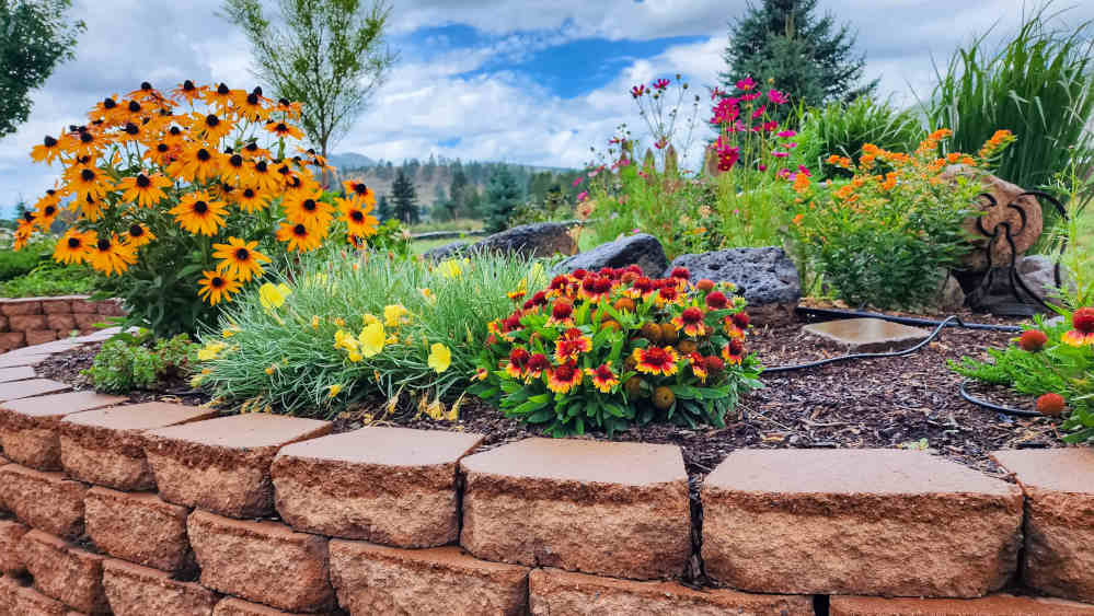 A raised block planter with native and pollinator attracting flowers in it.